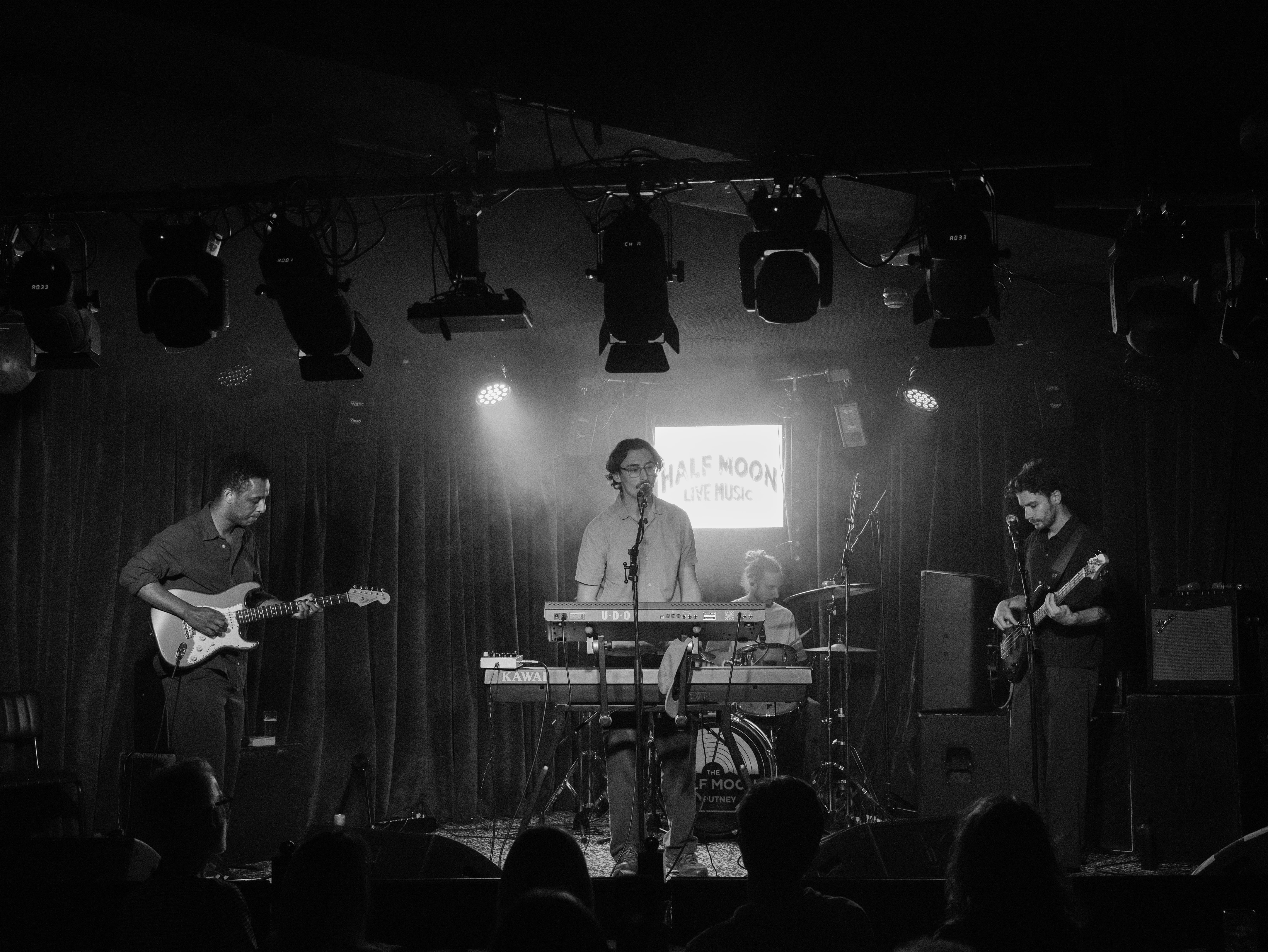 Black-and-white live show at The Half Moon Putney: four-piece band performing under stage lights for The Unsigned Guide